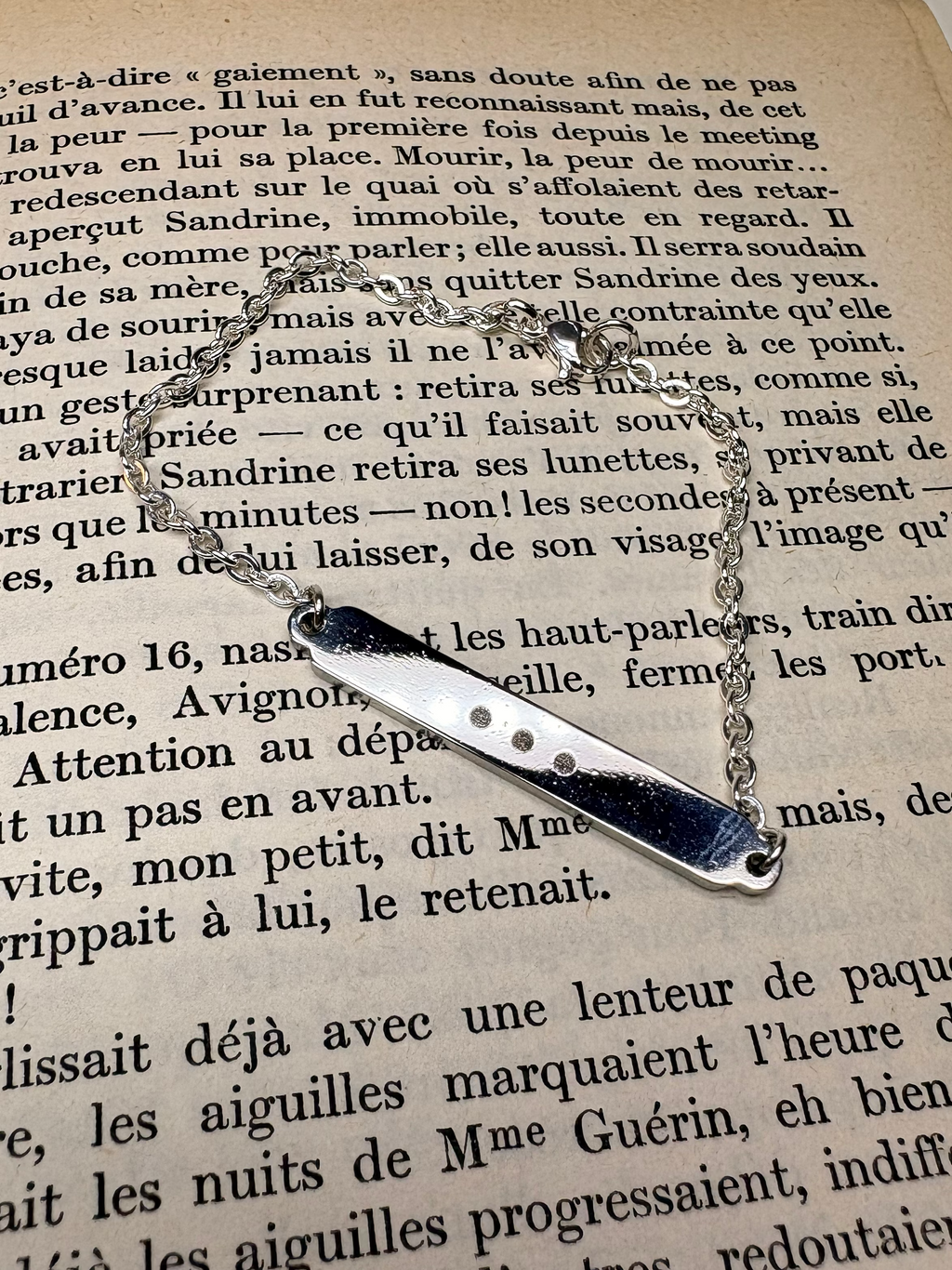 Armbandet ”Öppet slut” i rostfritt stål mot bakgrund med en bok 